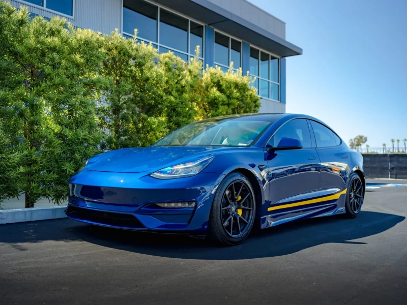 Blue Tesla model 3 standing by a building